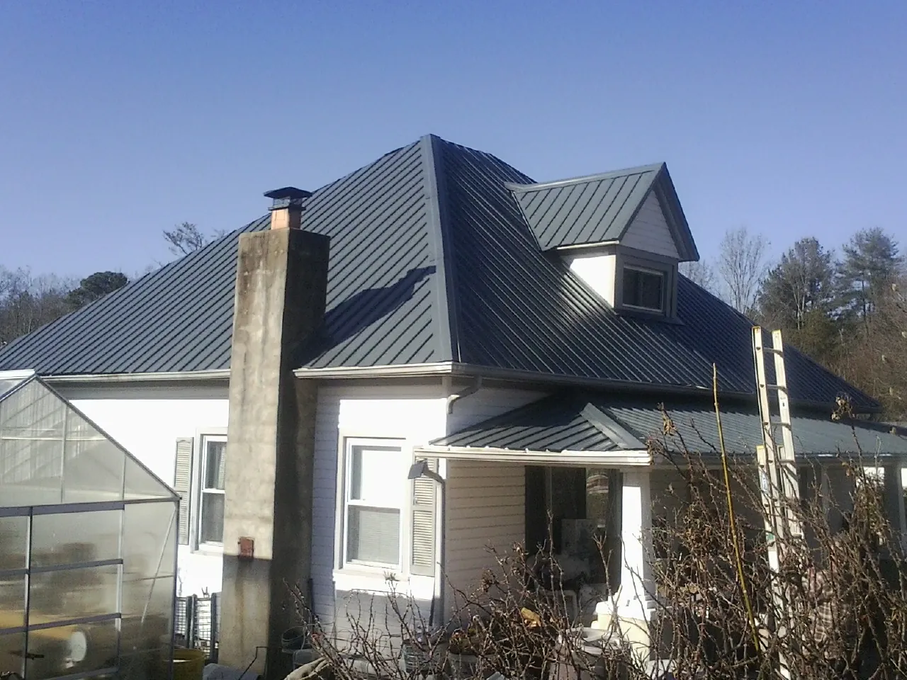 Dark blue standing seam metal roof on a white farmhouse with dormer — Slate & Tile Roof Repair by Roofing Brothers in Bowman