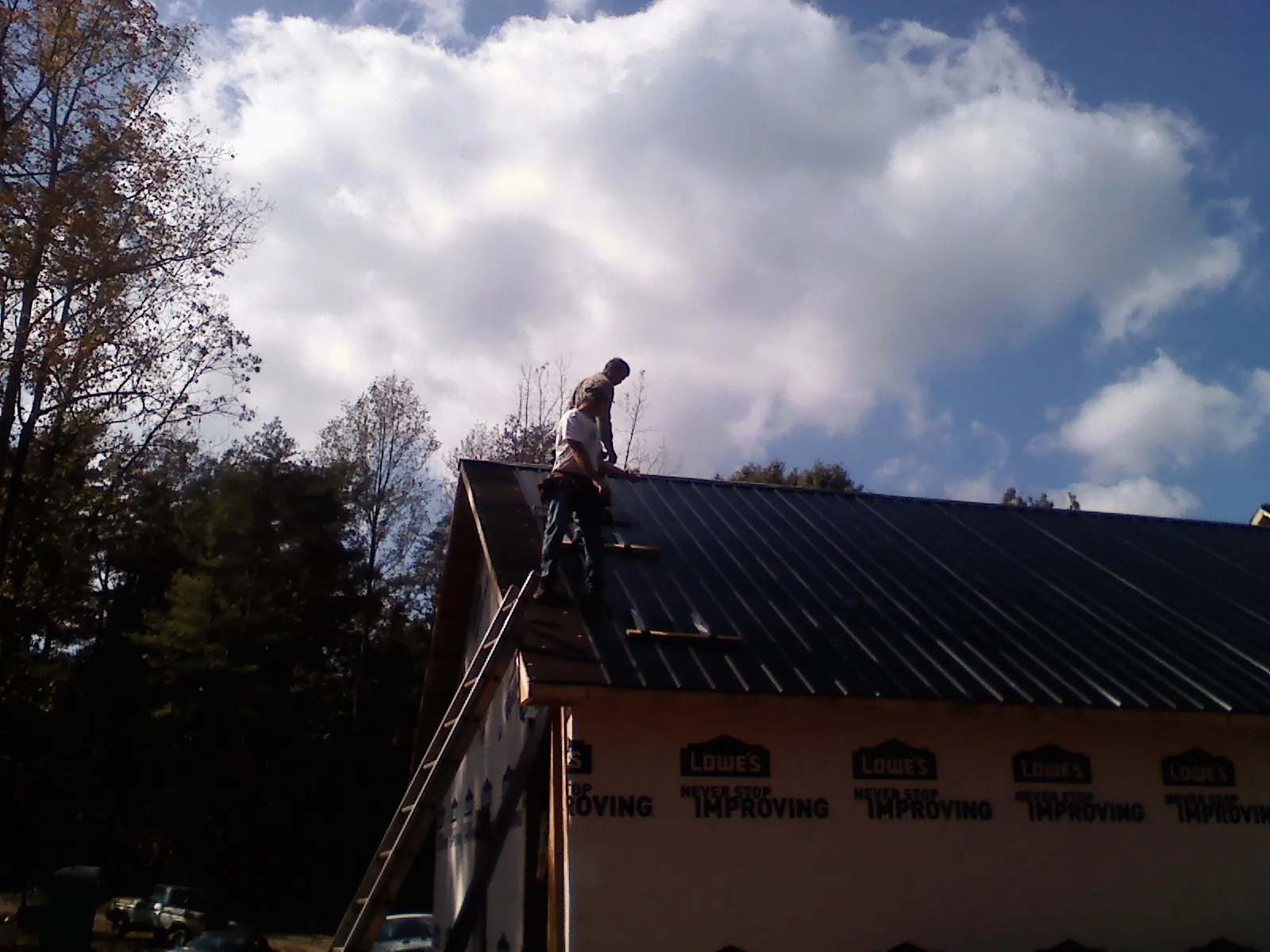Roofer fastening dark metal panels high against a cloudy sky, from a Roof Inspection job in Bowman