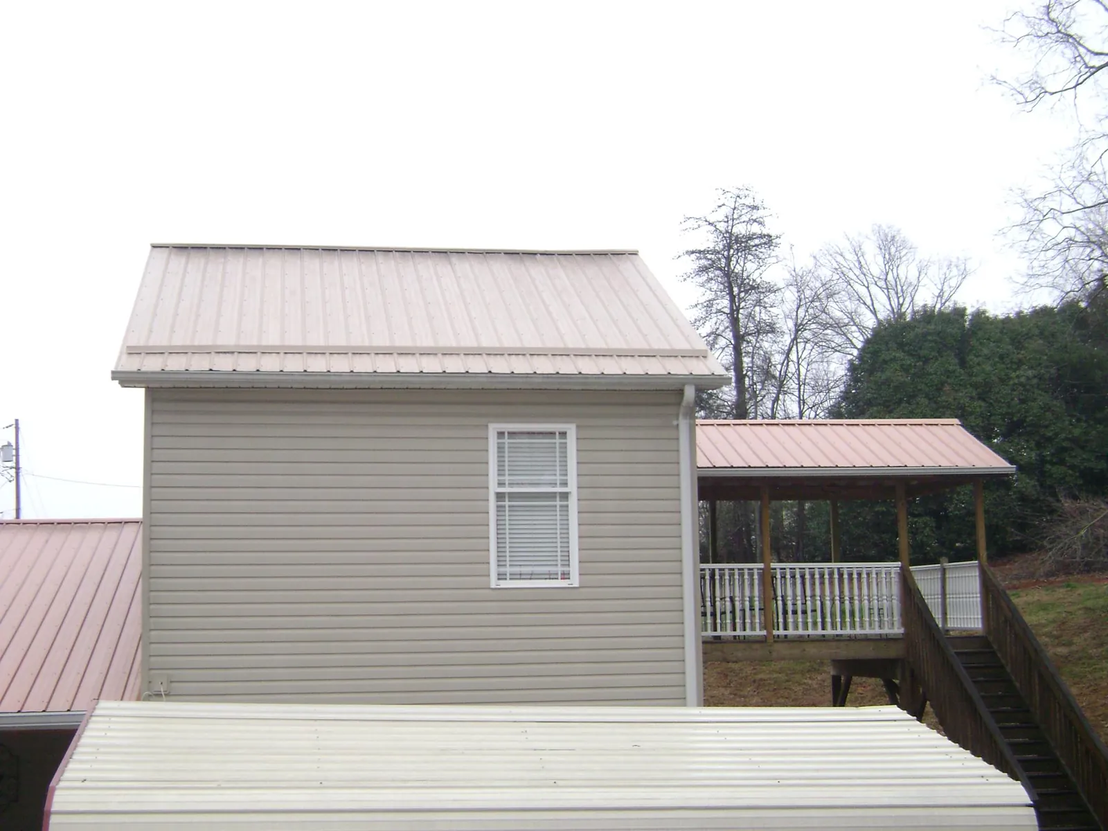 Tan metal roofs on a two story addition and attached porch, from a Roof Replacement job in Bowman